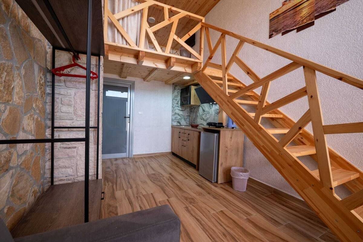 Una habitación estilo loft con escalera de madera, pared de piedra y zona de cocina.