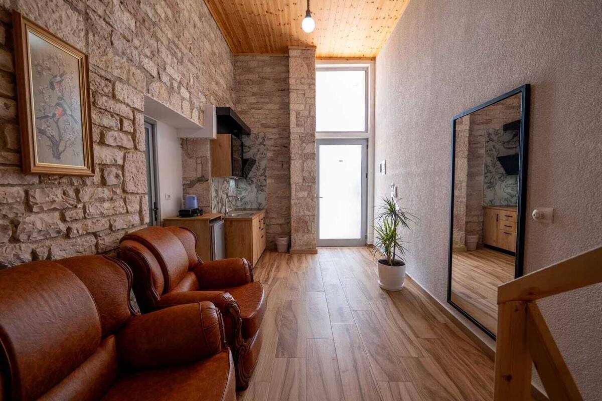 Una sala de estar con pared de piedra, suelo de madera, sofá de cuero, una planta en maceta y un espejo grande.