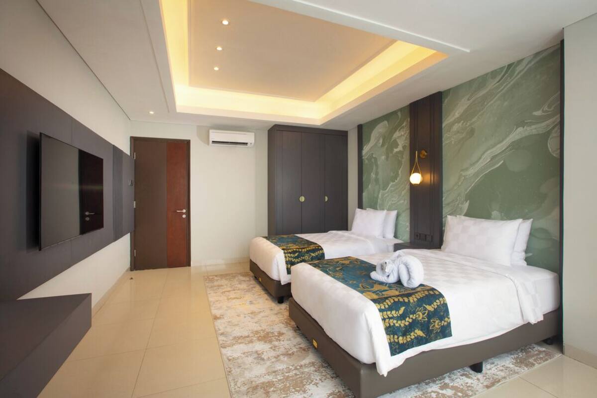 Habitación de hotel con dos camas, un televisor de pantalla plana, una lámpara de techo y una pared de mármol.