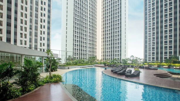 A swimming pool with lounge chairs, surrounded by tall residential buildings. - Louis Kienne Suite Cikarang (Cikarang)