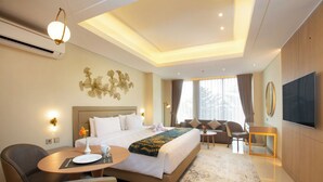 A modern hotel room with a large bed, a desk, a chair, a TV, and a window with curtains. - Louis Kienne Suite Cikarang (Cikarang)
