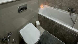 A modern bathroom with a bathtub, toilet, and vanity with a shelf holding toiletries.