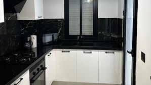 A modern kitchen with white cabinets, a black countertop, a stove, and a hanging light fixture.