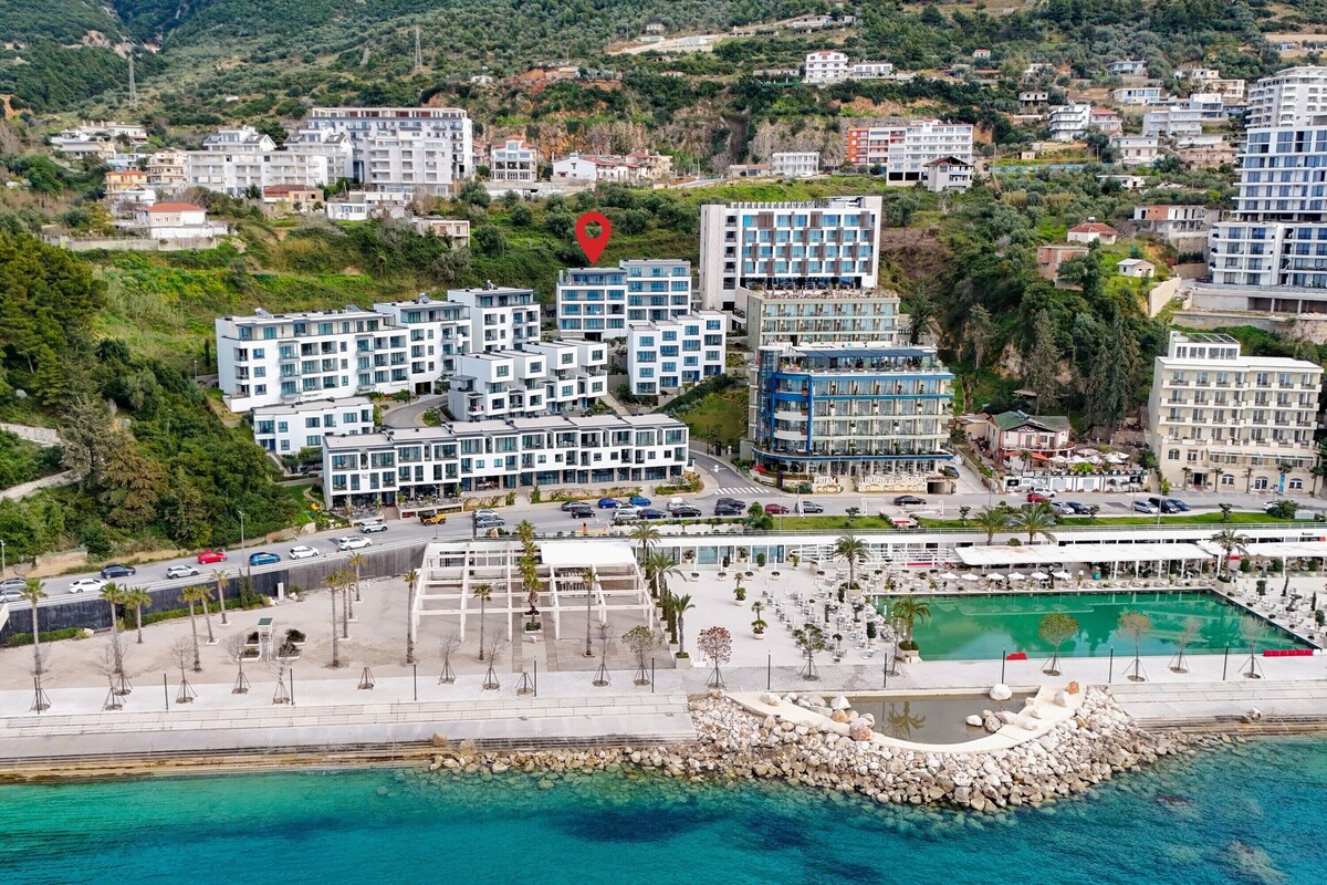 An aerial view of a coastal hotel with multiple buildings, a swimming pool, and a rocky shoreline.