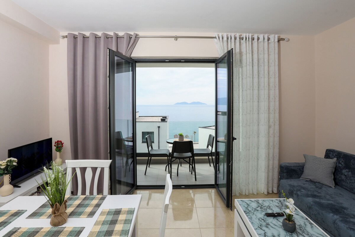A room with a balcony, a dining table, a sofa, and a TV.
