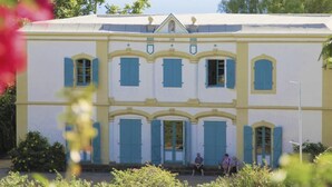 A large, two-story building with a symmetrical facade, multiple windows with shutters, and a central entrance. - Charming Cottage with Sea View and Jacuzzi in Saint-Paul (Le Guillaume)