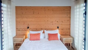 A bedroom with a wooden headboard, two bedside tables, and a bed with white bedding and two red pillows. - Charming Cottage with Sea View and Jacuzzi in Saint-Paul (Le Guillaume)