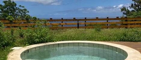Un jacuzzi en un jardín con una terraza de madera y vistas al océano.