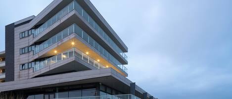 Un edifici modern d'àmbit vertical amb façana de vidre, zona d'estar a l'aire lliure i escala que condueix a l'entrada.