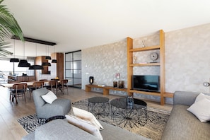 A modern living room with a sofa, coffee table, dining area, and TV. - Luxury North Sea Retreat With Garage (Egmond aan Zee)