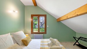 Un dormitorio con cama, almohadas, ventana, radiador y un banco.