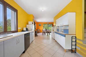 Une cuisine équipée d’un lave-vaisselle, une table à manger avec des chaises et une fenêtre donnant sur un espace verdoyant.