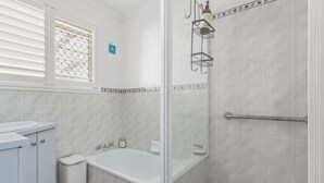 Et badeværelse med toilet, vask, badekar og bruser.