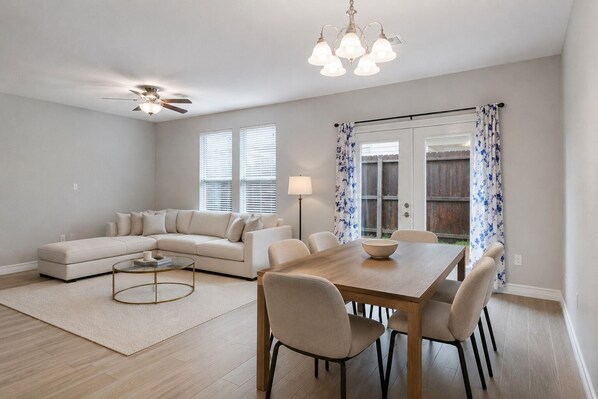 Ein modernes Wohnzimmer mit einem Ecksofa, einem Esstisch mit Stühlen, einem Couchtisch, einer Stehlampe und einem Deckenventilator.