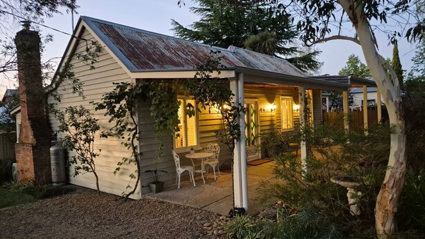 A small, single-story house with a sloped roof, a porch with chairs, and a garden area. - Finchy Cottage - Your charming Beechworth cottage where heritage character meets modern com (Beechworth)