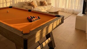 A pool table with balls, a sofa, a painting, and a television in a room with wooden flooring and white walls.