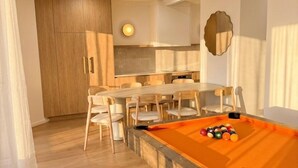 A modern living room with a pool table, wooden cabinets, and a dining area.