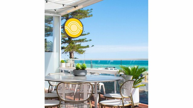 A patio with a round table and chairs, a potted plant, and a view of the ocean.
