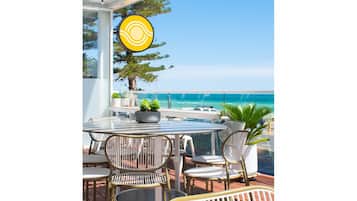 A patio with a round table and chairs, a potted plant, and a view of the ocean.