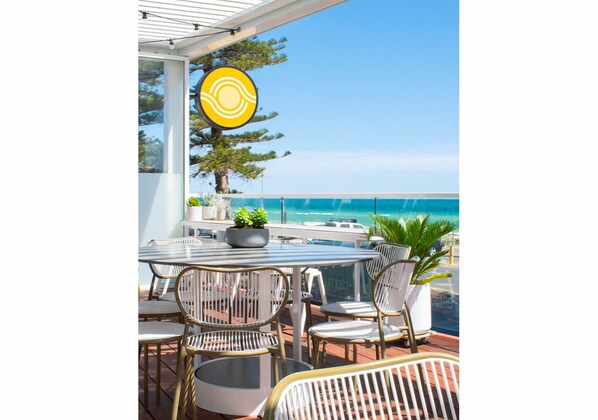 A patio with a round table and chairs, a potted plant, and a view of the ocean.