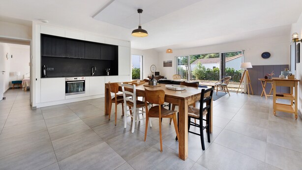 Une cuisine spacieuse équipée d’appareils modernes, un coin repas avec des chaises en bois et de grandes fenêtres offrant une vue sur l’extérieur.