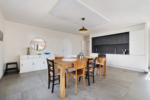 A modern kitchen with white cabinets, a wooden dining table, and a black countertop. - Maison des Orchidées just 100m from the beach (La Tranche-sur-Mer)