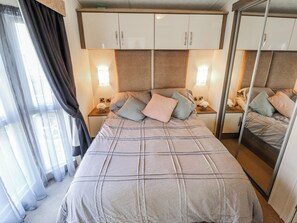 A bedroom with a bed, bedside tables, a mirror, and curtains. - 13 The Lakes (Mablethorpe)