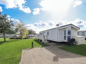 A mobile home with a paved driveway, a small attached garage, and a grassy yard with trees. - 13 The Lakes (Mablethorpe)