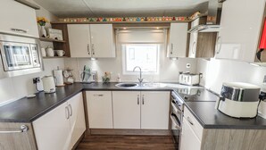 A modern kitchen with white cabinets, a wooden countertop, a built-in oven, a sink, and a window. - 13 The Lakes (Mablethorpe)