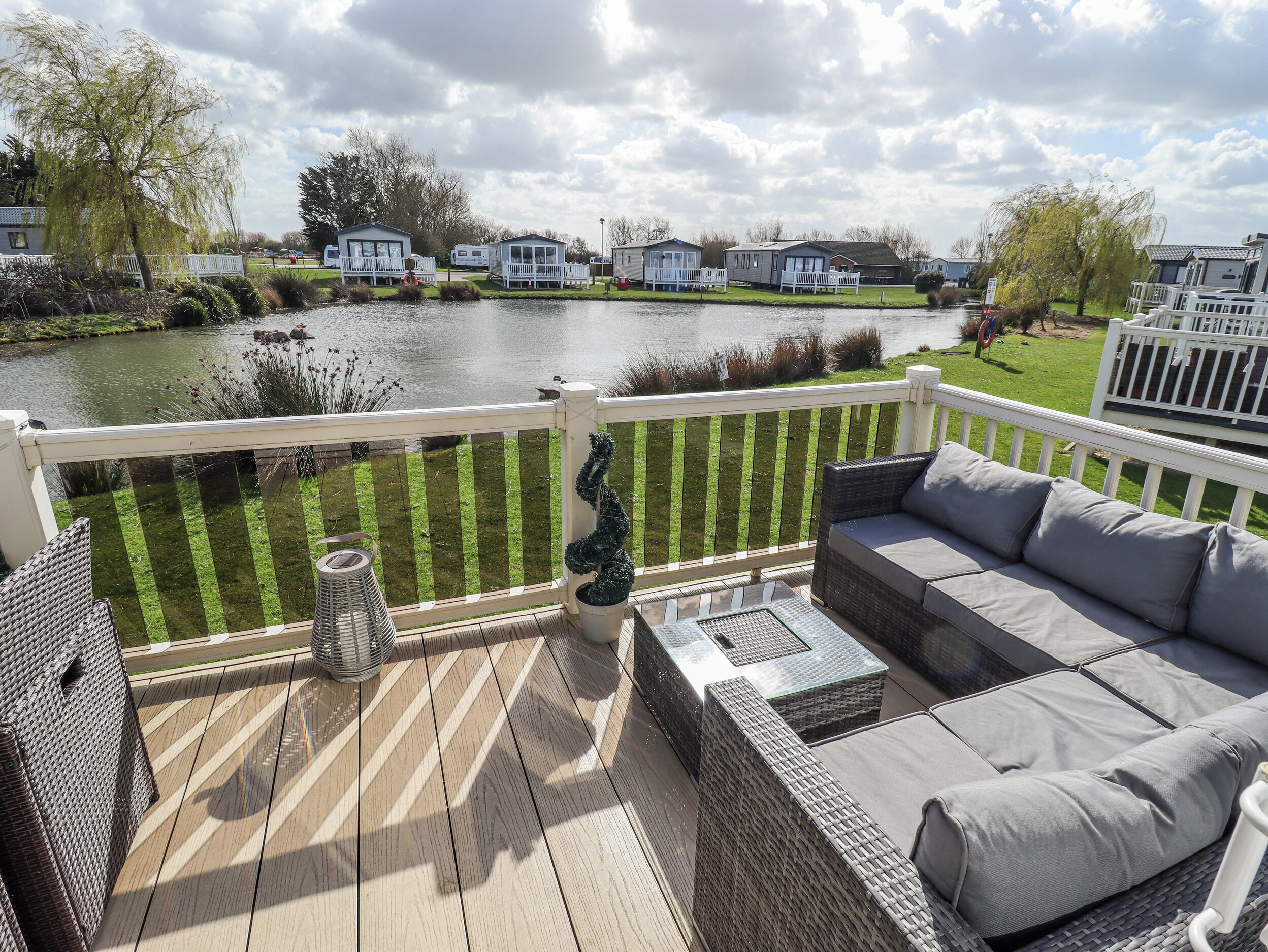 Une terrasse dotée de mobilier d’extérieur, avec vue sur un lac et des maisons mitoyennes en arrière-plan.