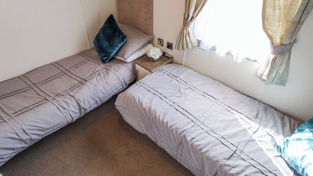 A room with two single beds, a nightstand, a lamp, and a window with curtains. - 13 The Lakes (Mablethorpe)