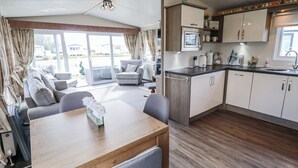 A modern kitchen with a microwave, sink, and cabinets. There is a dining area with a table and chairs. - 13 The Lakes (Mablethorpe)