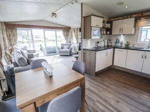 A modern kitchen with a microwave, sink, and cabinets. There is a dining area with a table and chairs. - 13 The Lakes (Mablethorpe)