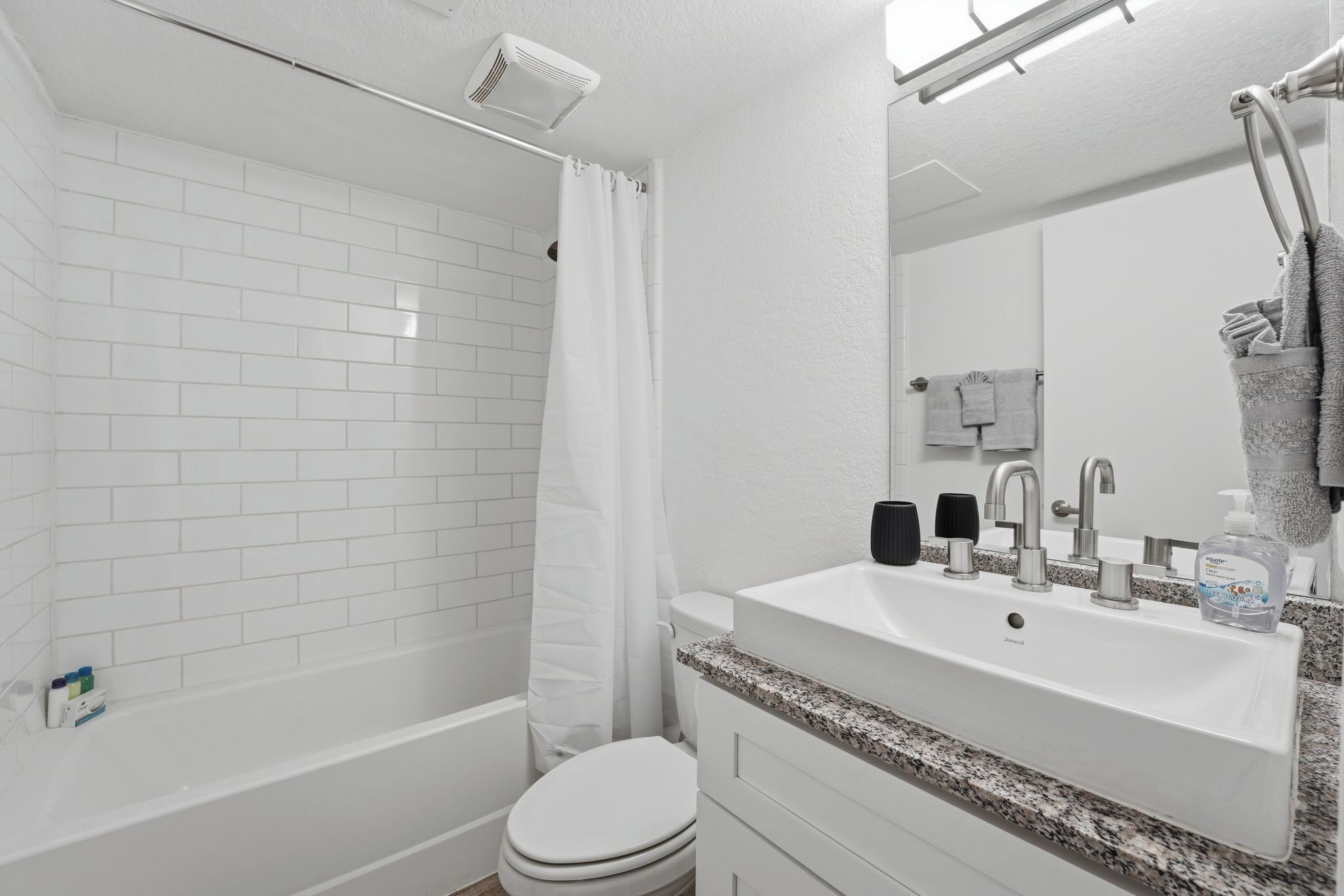 A modern bathroom with white tiles, a bathtub, a toilet, a sink with a mirror, and a towel rack.