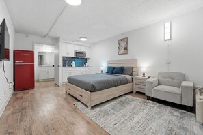 A modern bedroom with a bed, bedside table, chair, and a red refrigerator. - Modern Centro studio with cozy finishes (Austin)