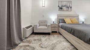 Un dormitorio con cama, mesitas de noche, una silla, un calentador y un cuadro en la pared.