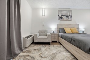 A bedroom with a bed, bedside tables, a chair, a heater, and a painting on the wall. - Functional studio with upgraded interiors (Austin)