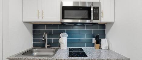 A compact kitchen with white cabinets, a stainless steel microwave, a built-in oven, a sink, and a stovetop.