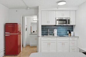 A compact kitchen with white cabinets, a red refrigerator, a microwave, and a blue-tiled backsplash. - Comfortable studio with updated amenities (Austin)