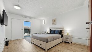 Une chambre à coucher comprenant un lit, des tables de chevet, un téléviseur et une porte donnant sur un balcon.