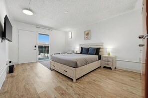 A bedroom with a bed, bedside tables, a TV, and a door leading to a balcony. - Contemporary Centro Flats studio getaway (Austin)