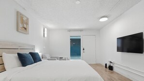 Ein modernes Hotelzimmer mit einem großen Bett, einem Flachbildfernseher, Holzboden und einer Tür zu einem Balkon.