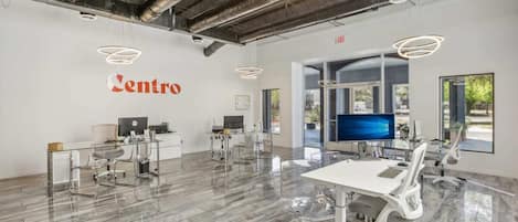 A spacious, modern office with a glass desk and chairs, a large monitor, and a sign reading "Centro" on the wall.