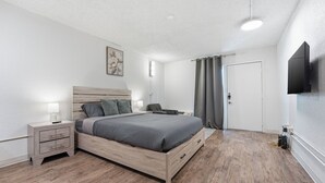 Een slaapkamer met een bed, nachtkastjes, een televisie, een deur en een gordijn.