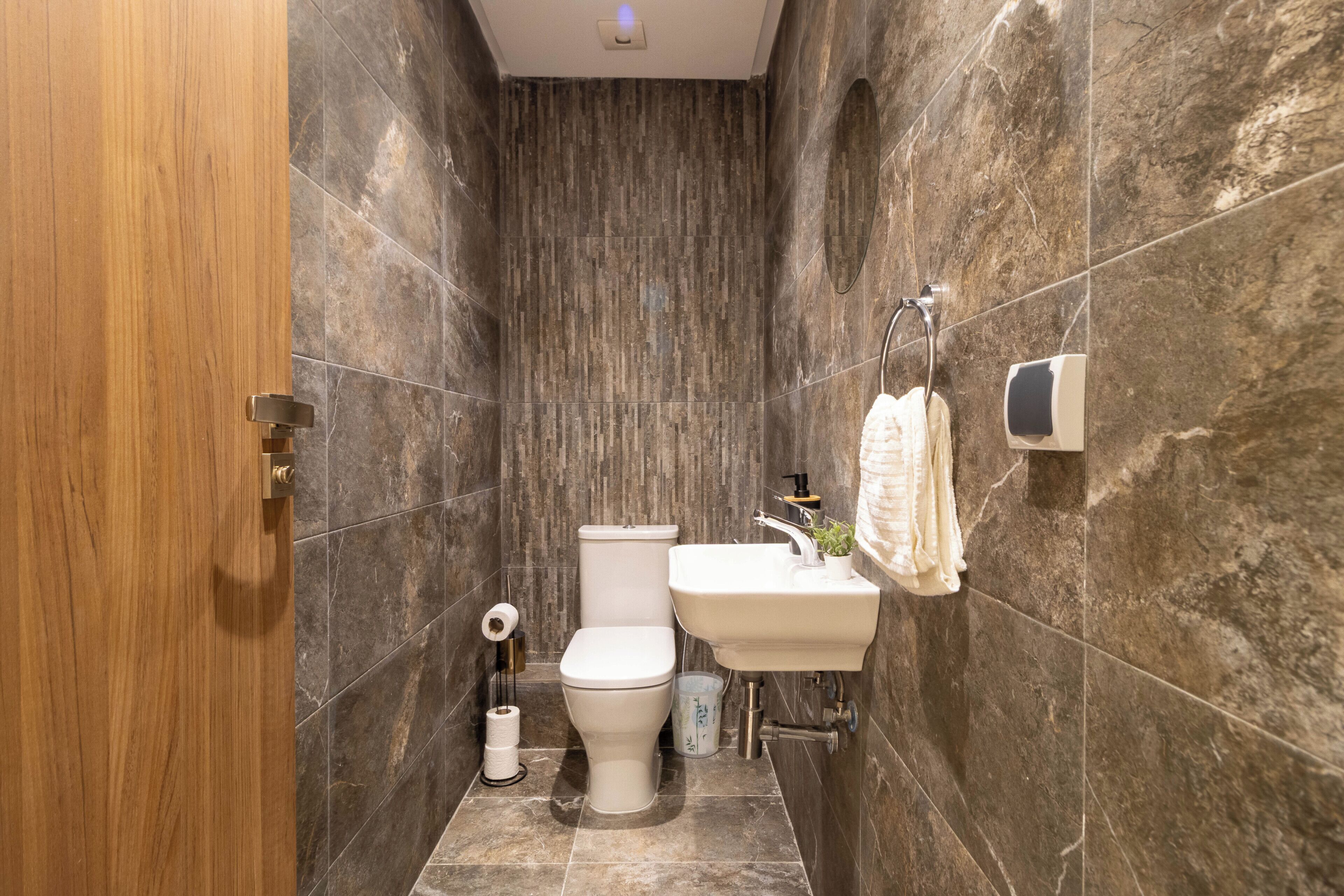 A bathroom with a wooden door, a toilet, a sink, and a towel rack.