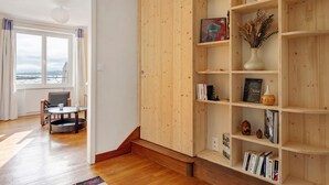 Ein Zimmer mit einer Holzbücherwand, einem Esstisch mit Stühlen und Blick durch ein Fenster.