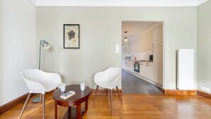 Ein Zimmer mit Holzboden, einem Esstisch mit zwei Stühlen, einer Stehlampe und einem gerahmten Bild an der Wand.