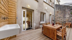 Eine Holzterrasse mit Tisch, Stühlen, einem Spülbecken und einer Steinmauer.