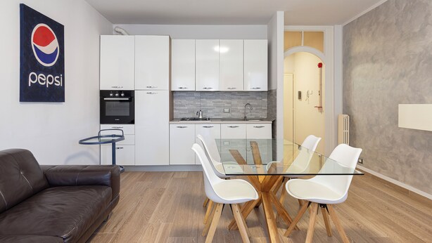 A modern kitchen with white cabinets, a glass dining table with white chairs, and a brown leather sofa. - The house of the badger (Feriolo)