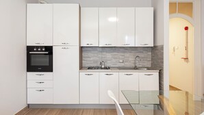 A modern kitchen with white cabinets, a black oven, and a glass dining table. - The house of the badger (Feriolo)